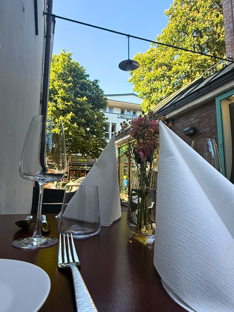 Stilvoll gedeckter Tisch im Außenbereich mit weißen Servietten, Gläsern und Blumendekoration